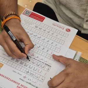Jemand schreibt chinesische Schriftzeichen auf einem Übungsblatt.